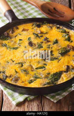 Italian omelette with spinach, cheddar cheese and mushrooms in a pan close-up on the table. vertical Stock Photo