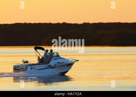 Dawn greets two men on a boat on Pumicestone Passage off Golden Beach, Caloundra on the Sunshine Coast of Queensland, Australia. Stock Photo