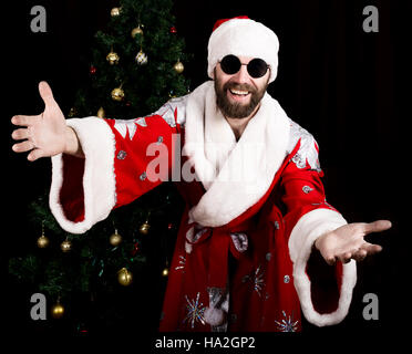 bad rastoman Santa Claus smiles and spread his hands in different side on the background of Christmas tree Stock Photo