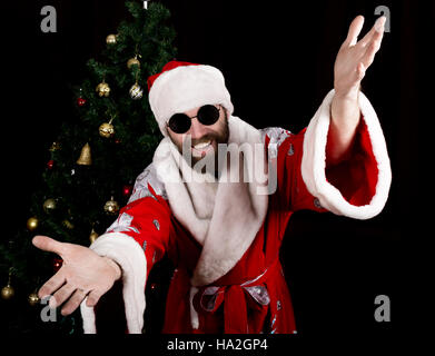 bad rastoman Santa Claus smiles and spread his hands in different side on the background of Christmas tree Stock Photo