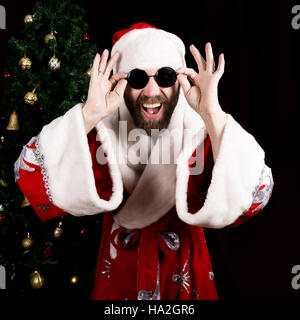 bad rastoman Santa Claus holds round glasses and smiles, on the background of Christmas tree. different funy emotions Stock Photo