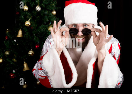 bad rastoman Santa Claus holds round glasses and smiles, on the background of Christmas tree. different funy emotions Stock Photo