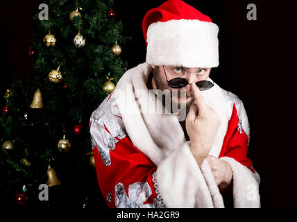 bad rastoman Santa Claus holds round glasses and smiles, on the background of Christmas tree. different funy emotions Stock Photo