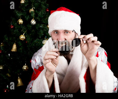 bad rastoman Santa Claus holds round glasses and smiles, on the background of Christmas tree. different funy emotions Stock Photo