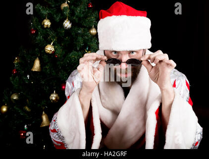 bad rastoman Santa Claus holds round glasses and smiles, on the background of Christmas tree. different funy emotions Stock Photo