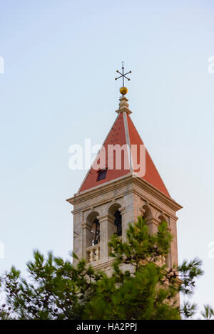 Christian church steeple in front of pines on blue sky with red roof and cross on top Stock Photo