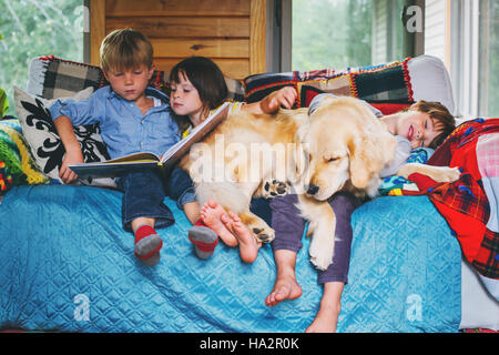 Three children sitting on couch reading together with dog Stock Photo