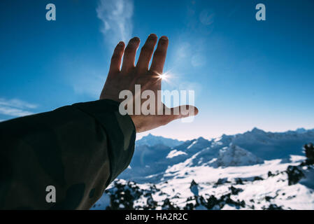 Man's hand reaching for sun in mountains Stock Photo