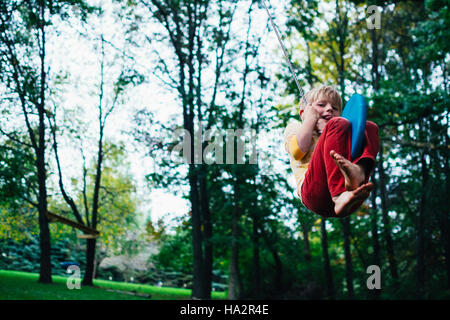 Boy swinging on a rope swing in the garden Stock Photo
