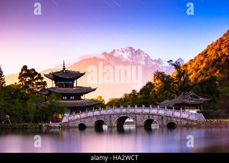 Star trails curl over Black Dragon Pool as Jade Snow Dragon Mountain looms in the background in the city of Lijiang, Yunnan Province, China Stock Photo