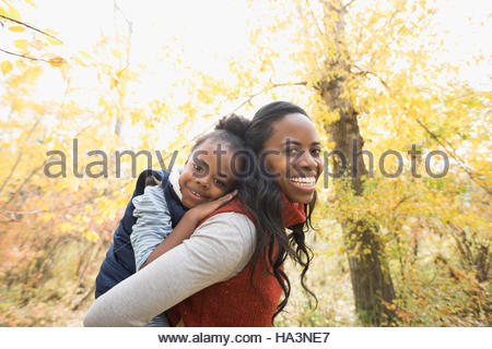 Portrait smiling mother piggybacking daughter in autumn woods Portrait smiling mother piggybacking daughter in autumn woods