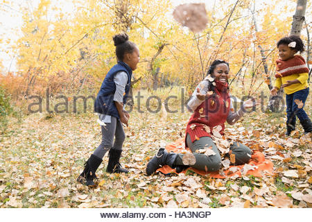 Mother and daughters playing throwing autumn leaves in park