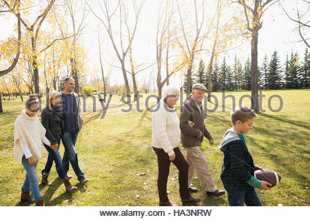 Multi-generation family walking with football in sunny autumn park