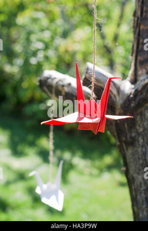 Origami cranes in the garden. Figures of paper in the nature. Red and white cranes on tree. Stock Photo