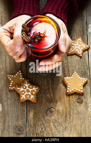 Christmas hot drink - mulled wine in female hands with cinnamon stick, star anise and festive Christmas gingerbread cookies over rustic wooden backgro Stock Photo