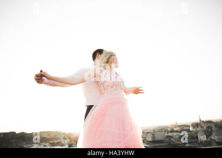 Young couple in love posing on roof with perfect city view holding hands and hugging . Beautiful sunset