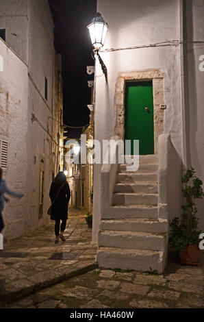 A woman walks down a narrow alleyway at night in Ostuni, Puglia, Italy Stock Photo