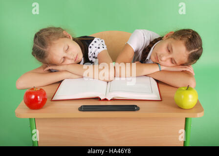 Two school girls sleeping on a stack of books at her desk isolated on green Stock Photo