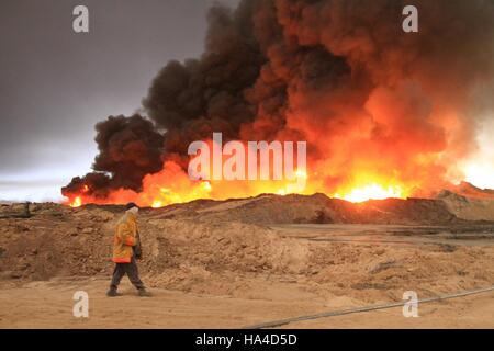 Qayyarah, Iraq. 26th November, 2016. An oil company worker walks near burning oil wells in Qayyarah town, south of Mosul, in northern Iraq, on Nov. 26, 2016. Qayyarah town is seized by the Islamic State (IS) militants in June of 2014. The IS militants bombed all oil wells here when Iraqi army recaptured the town in August this year. The army started military operations to retake Mosul city on Oct. 17, since when the government organized oil companies to put off the fire. Credit:  Xinhua/Alamy Live News Stock Photo