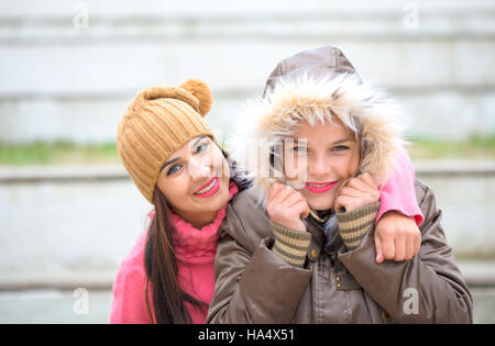 Two cheerful cute girls, one hugging  her best female friend outdoors in winter Stock Photo