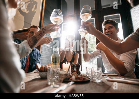 Group of young people making a toast at restaurant. Men and women sitting at a table in cafe and toasting wine. Stock Photo