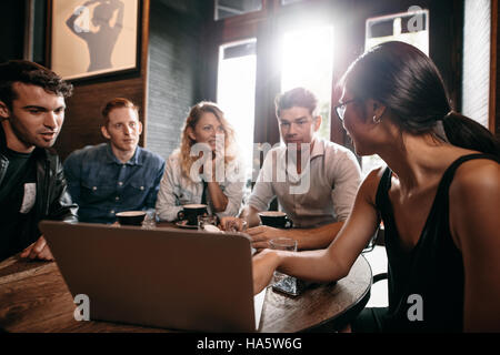 Smiling friends spending their time in coffee shop and discussing something while looking at laptop. Woman showing something to her friends sitting at Stock Photo
