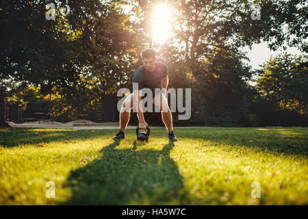 Shot of fit young man exercising with kettlebell outdoors in the park.  Strong young guy training at park in morning. Stock Photo
