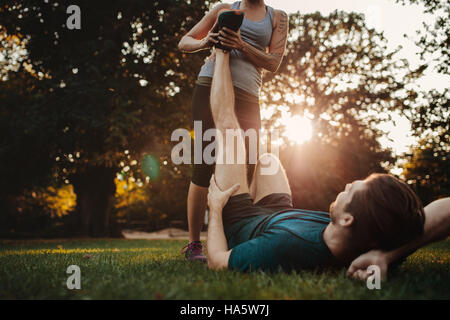 Young man having a strain and being stretched by female trainer. Woman stretches man's leg, muscle spasm after sport training. Stock Photo