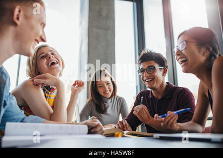 Multiethnic young people sitting at table and having fun while studying together for exams. Group of happy young students in library. Stock Photo