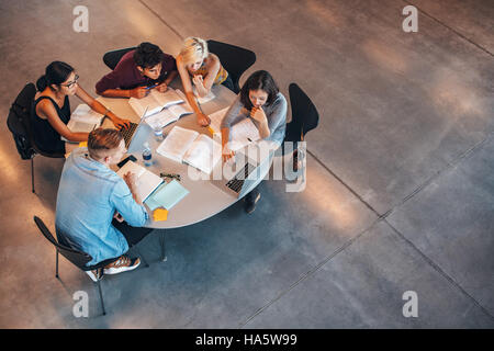 Multiracial group of young students studying together. High angle shot of young people sitting at the table and studying on laptop computer. Stock Photo