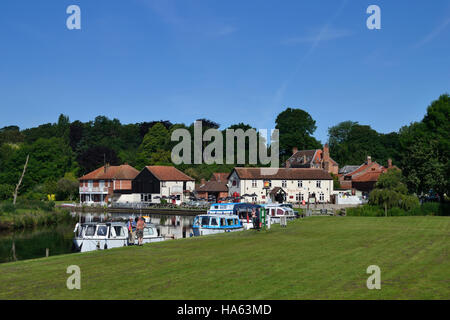 Boats moored at the staithe on the River Bure at Coltishall Common with the Rising Sun pub beyond on the Norfolk Broads. Stock Photo