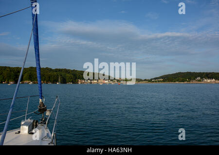 View of Dale village with a yacht's bow anchored in the bay. Blue summer sky with white clouds, blue sea with ripples. Stock Photo