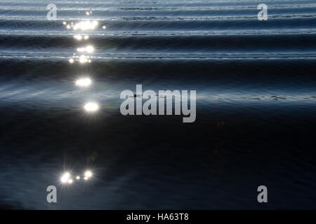 Sunlight making stars on boat wake creating an interesting pattern of waves on blue rippled water. Stock Photo