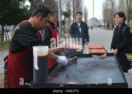 Tokyo, Japan-2/26/16: Two street food vendors grilling yakitori chicken on a portable flat skillet grill while two customers wait for their order. Stock Photo