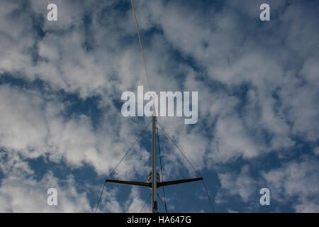 Looking up a yacht's mast against blue sky with fluffy white clouds. In landscape format.