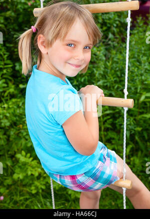Portrait of cute little girl playing on a rope ladder in a summer park Stock Photo