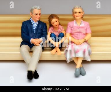 An elderly senior miniature figurine couple sitting on a bench with their granddaughter Stock Photo