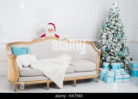 Santa Claus hiding behind a sofa over home interior Stock Photo