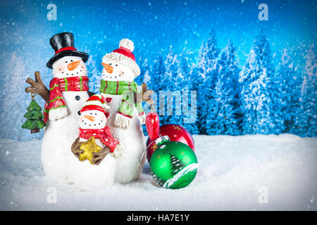 Christmas decoration with snowman figurines as a family, colorful baubles on a blue snow pine tree landscape background. Stock Photo