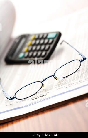 Pair of glasses on top of stock quotations with calculator, symbolic picture Stock Photo