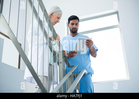 Doctors discussing over digital tablet while standing on stairs Stock Photo