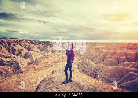 Vintage toned photo of a female photographer taking pictures at sunset, Badlands National Park, South Dakota, USA.