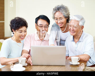 four senior asian people gathering at home using laptop computer together. Stock Photo