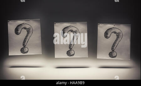 Question marks drawn on paper, on gray background. Stock Photo