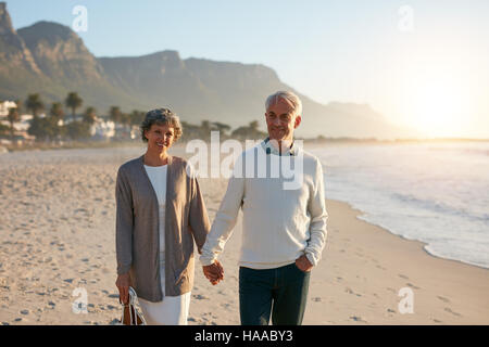Portrait of a happy senior couple taking a walk on the beach together. Mature couple holding hands and walking on the sea shore. Stock Photo