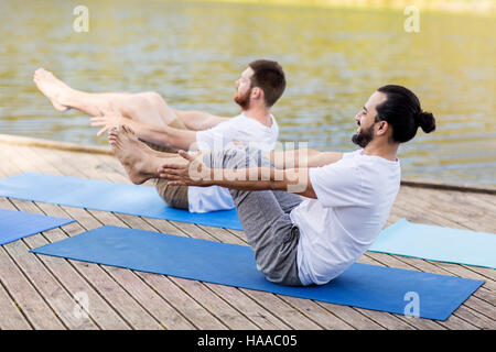 men making yoga in half-boat pose outdoors Stock Photo