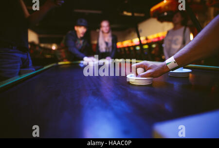 Young friends playing air hockey game at amusement park, focus on hand of man holding striker. Stock Photo