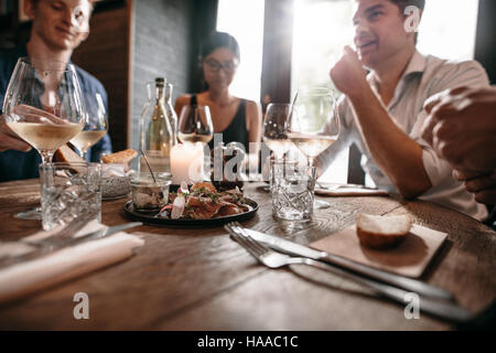 Group of friends meeting at cafe with glasses of wine on table. Men and women having a dinner at restaurant. Stock Photo