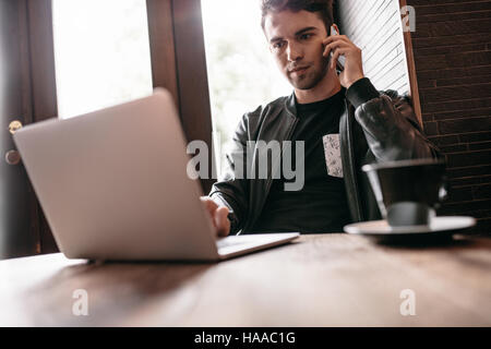 Handsome man sitting in cafe table with cup of coffee using mobile phone and laptop. Stock Photo