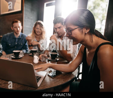 Group of friends in cafe watching something online on laptop. Young men and women at restaurant looking at laptop. Stock Photo